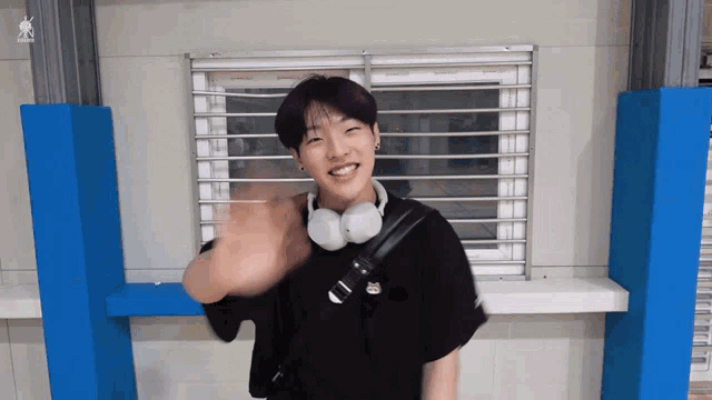 a young man wearing headphones and a black shirt is waving his hand in front of a window