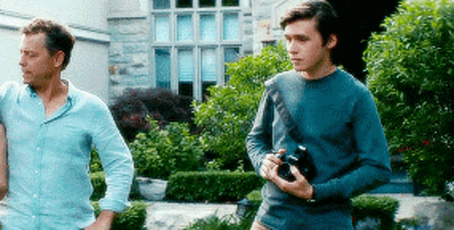 a man holding a camera stands next to another man in front of a house .