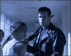 a man in a leather jacket is holding a gun to a woman 's face .