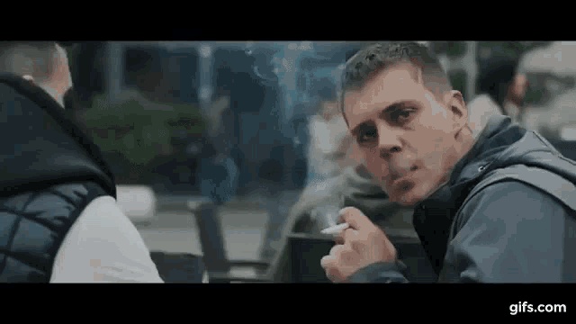 a man is sitting at a table smoking a cigarette .