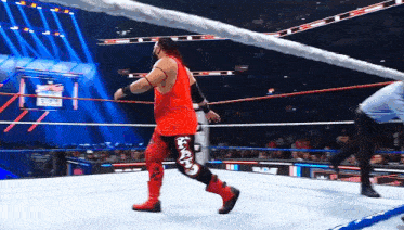 a wrestler in a red shirt and black pants is walking out of a ring