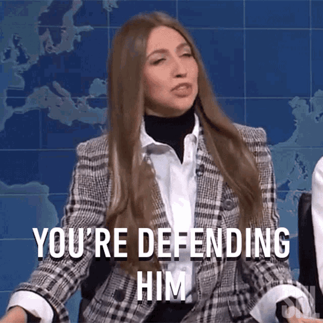 a woman in a plaid jacket is sitting in front of a map and says you 're defending him .