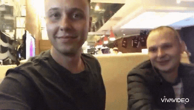 two men are posing for a selfie in a restaurant and the words vivavideo are on the bottom right