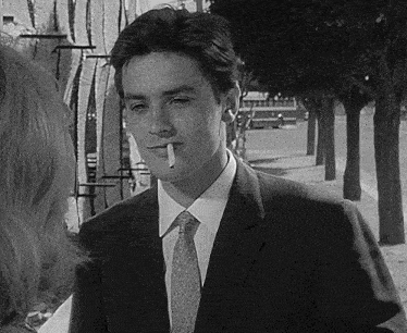 a man in a suit and tie is smoking a cigarette and talking to a woman .