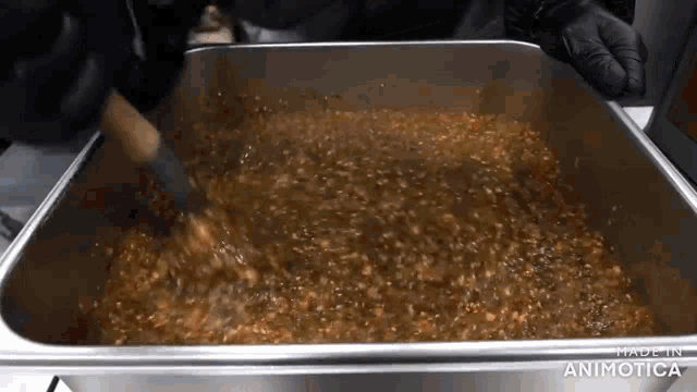 a pan of food is being stirred with a wooden spoon and the words made in animatica are on the bottom