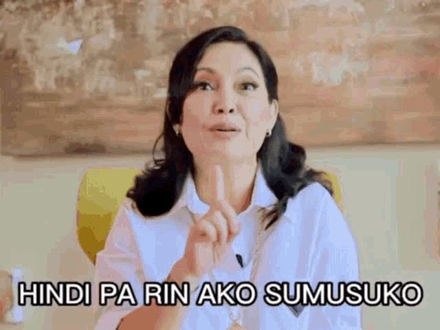 a woman in a white shirt is sitting in a chair and making a funny face with her finger up .
