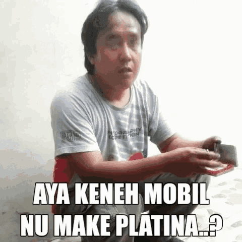 a man is sitting on the ground holding a wallet and a cell phone and says aya kenah mobil nu make platina ?