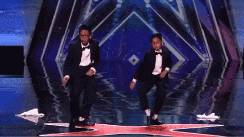 two young men in tuxedos are dancing on a stage