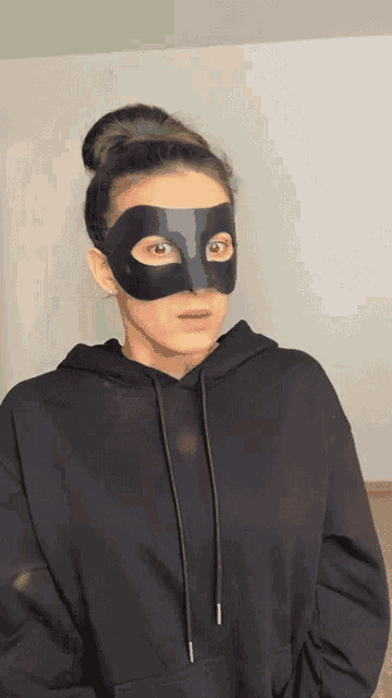 a woman wearing a black hoodie and a black mask with red eyes