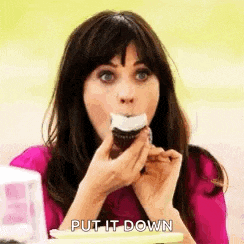 a woman in a pink shirt is eating a cupcake with a white frosting on it .