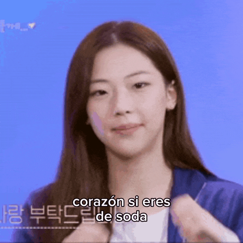 a woman with long hair is wearing a blue jacket and says corazón si eres de soda in spanish .