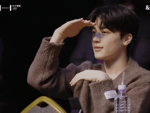 a young man wearing a brown sweater has a label on his shirt that says ' seouls ' on it