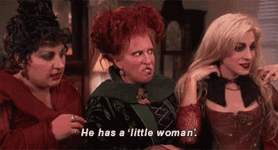 three women are standing next to each other in a room and one of them is saying `` he has a little woman . ''