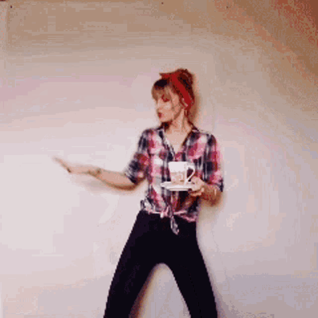 a woman in a plaid shirt and black pants is holding a cup of coffee