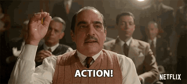 a man with a mustache is holding a pencil in his hand and says action