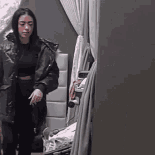 a woman in a black jacket is standing in a room with a clock on the wall .