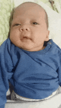 a baby in a blue shirt is laying on a white blanket