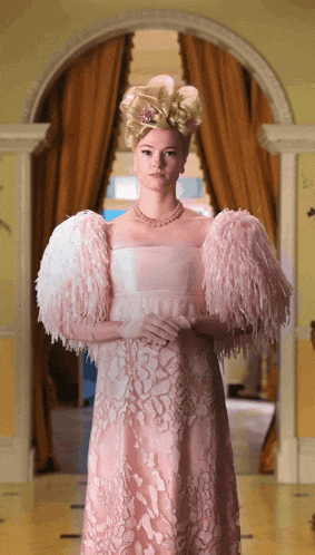 a woman in a pink dress with feathered sleeves is standing in a hallway