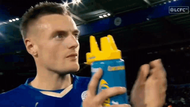 a man in a blue shirt is holding a blue and yellow bottle