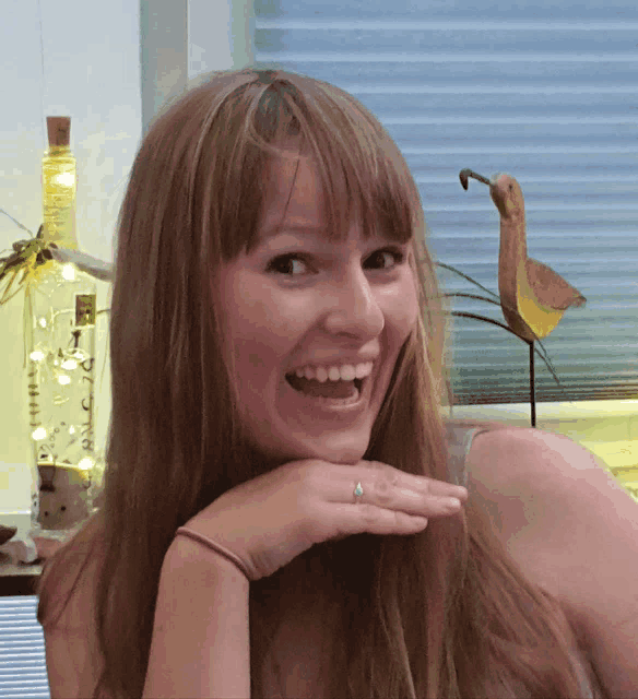 a woman with a ring on her finger smiles with a bird in the background