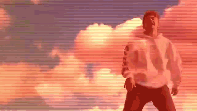 a man in a white sweatshirt is standing in front of a cloudy sky .