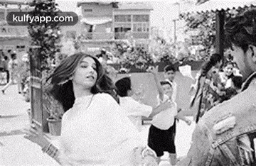 a black and white photo of a woman dancing in front of a crowd of people .