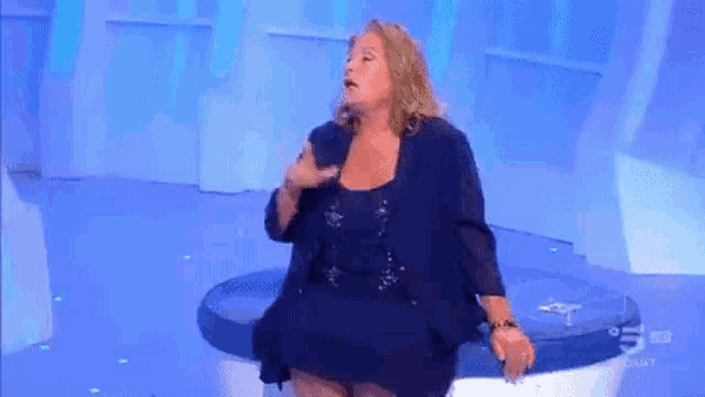 a woman in a blue dress is sitting on a blue couch on a television show .
