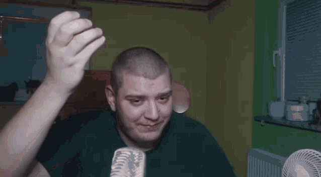 a man in a green t-shirt is standing in front of a fan .