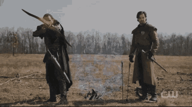 two men standing in a field with a cw logo on the bottom right