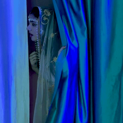 a woman in a blue and white dress is peeking out of a blue curtain