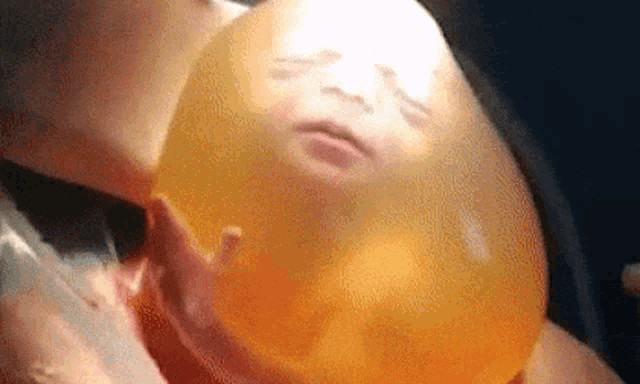 a close up of a baby 's face inside of a large orange balloon .