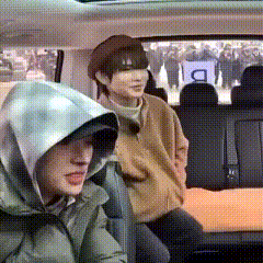 two people are sitting in the back seat of a car . one of the people is wearing a hooded jacket .