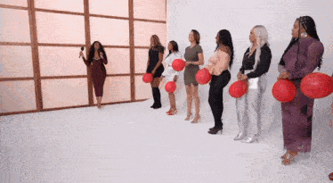 a group of women standing in a row holding red balloons .