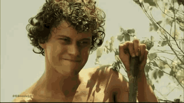a shirtless man with curly hair is holding a stick in his hand