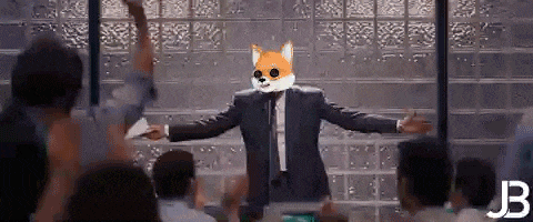 a man in a suit and tie with a fox mask on his face is giving a speech to a crowd of people .