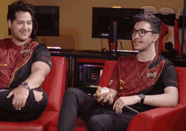 a man wearing a red and black shirt that says kings sits next to another man