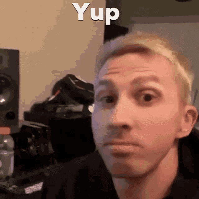 a man with blonde hair is making a funny face in a room with speakers in the background .