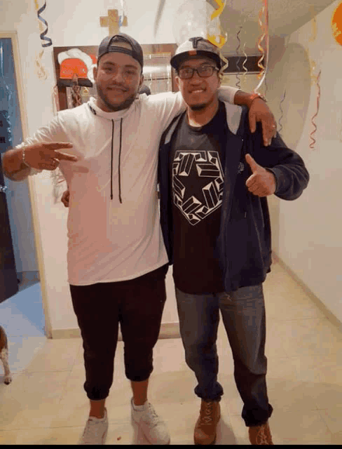 a man wearing a black shirt with a star on it stands next to another man wearing a white hoodie