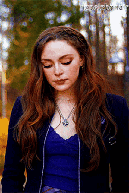 a woman with long red hair wearing a blue top and a necklace