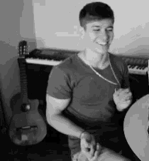a black and white photo of a man sitting at a table with a guitar and keyboard in the background