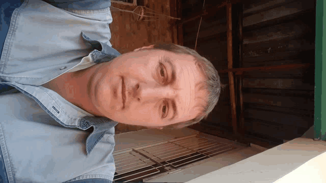 a man in a denim shirt is looking down at the camera