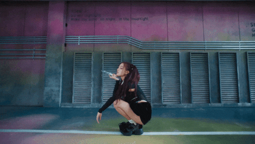 a woman is squatting down in front of a pink wall that says ' rising ' on it