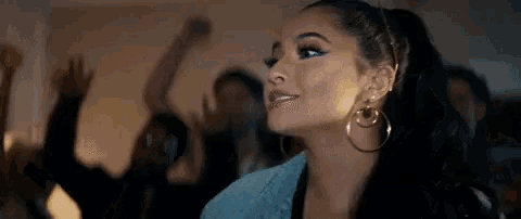 a woman wearing hoop earrings and a ponytail is standing in front of a crowd at a party .