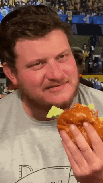 a man is eating a hamburger with lettuce and a shark on his shirt