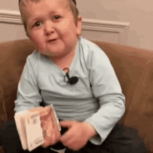 a little boy is sitting on a couch holding a book of money .