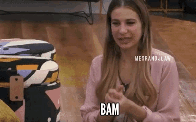 a woman in a pink shirt is sitting on the floor and says bam