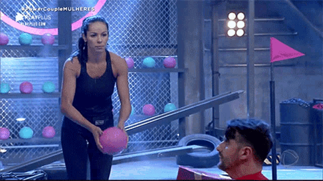 a woman in a black tank top holds a pink ball in front of a man