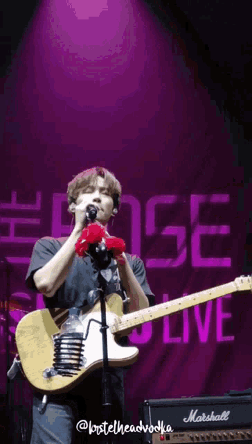 a man singing and playing a guitar in front of a sign that says live