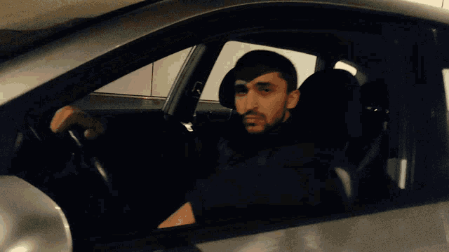 a man with a beard is sitting in the driver 's seat of a silver car