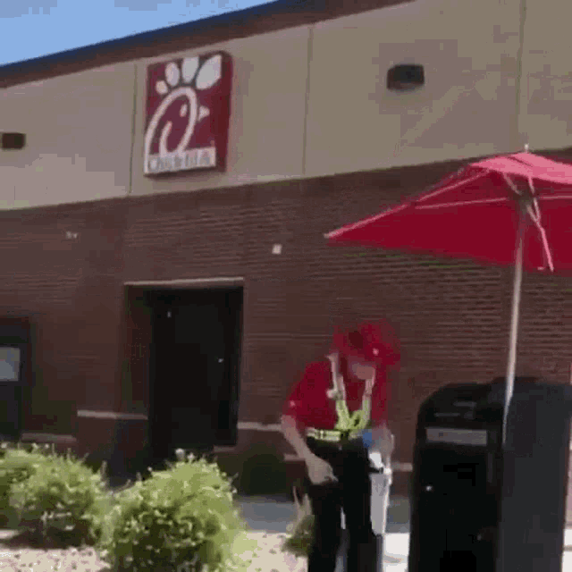 a man in a red uniform is standing in front of a chick-fil-a restaurant .